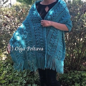 May include: A teal crochet shawl featuring an intricate openwork pattern and a long fringe along the bottom edge. The garment is draped over the shoulders and includes the text (c) Olga Poltava printed on the left side of the fabric.