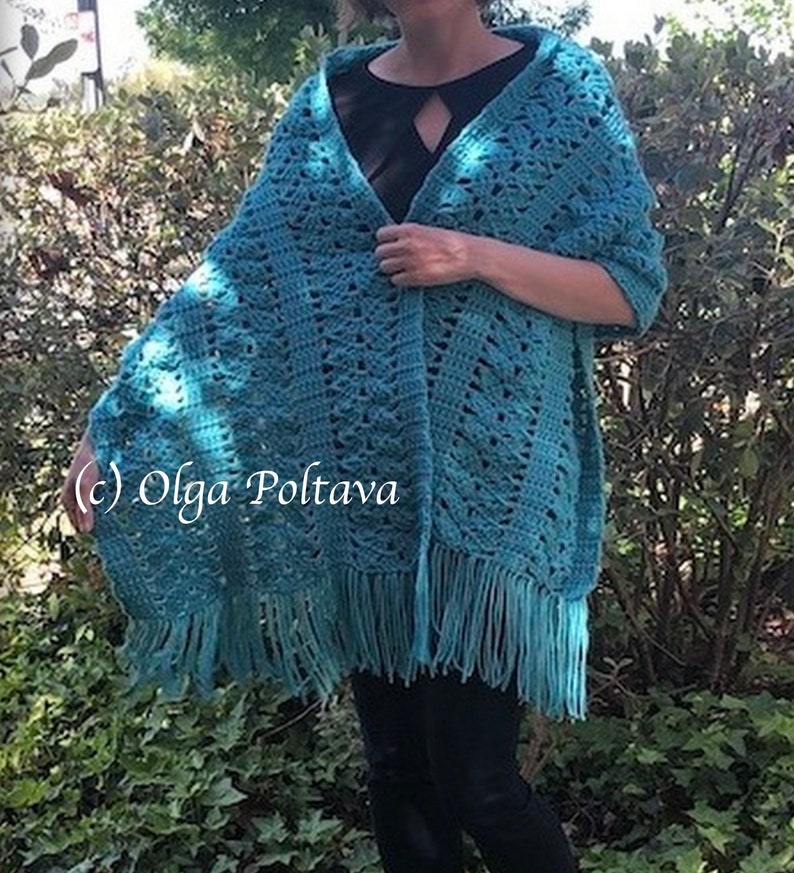 May include: A teal crochet shawl featuring an intricate openwork pattern and a long fringe along the bottom edge. The garment is draped over the shoulders and includes the text (c) Olga Poltava printed on the left side of the fabric.