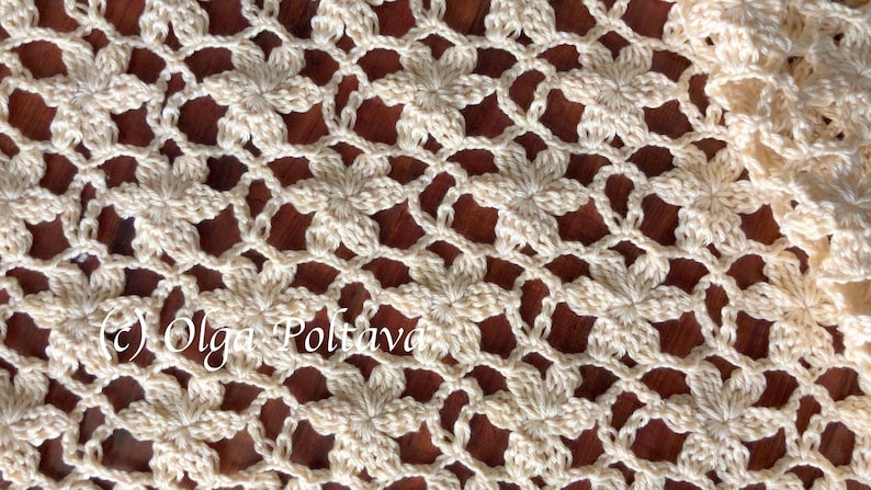 May include: A close-up of a crocheted doily with a delicate floral pattern in a cream color. The doily is laid out on a wooden surface.