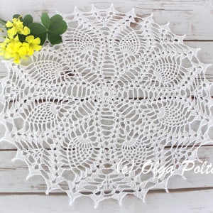 Op de afbeelding: Een rond wit gehaakt kleedje met een ingewikkeld, op ananas geïnspireerd patroon met een puntige, geschulpte rand. Het delicate textielwerk toont een symmetrisch ontwerp dat vanuit het midden uitstraalt. De tekst (c) Olga Poltava is zichtbaar.