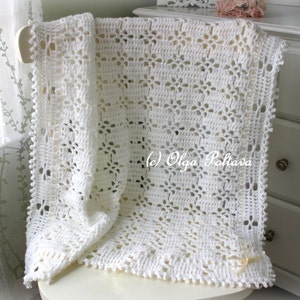 May include: White crocheted baby blanket with a delicate floral pattern. The blanket is draped over a white chair and has a small white bow on the corner.