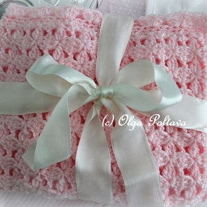 May include: A pink crocheted baby blanket with a white satin ribbon tied in a bow. The blanket has a delicate floral pattern.