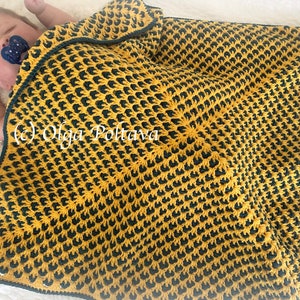 Puede incluir: Una manta de beb&eacute; de crochet amarilla y verde con un patr&oacute;n repetitivo. La manta est&aacute; doblada sobre un beb&eacute;.