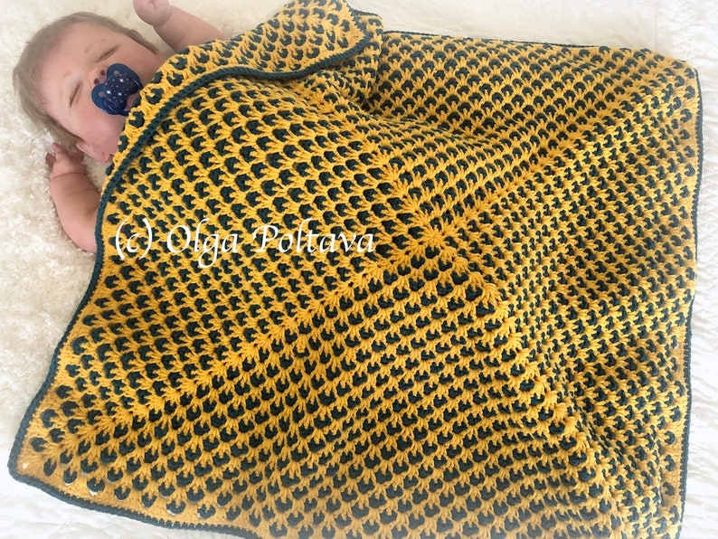 Puede incluir: Una manta de beb&eacute; de crochet amarilla y verde con un patr&oacute;n repetitivo. La manta est&aacute; doblada sobre un beb&eacute;.