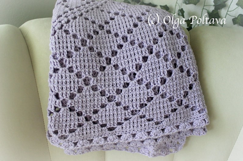 Puede incluir: Una manta de ganchillo de color lavanda con un delicado patr&oacute;n de encaje. La manta est&aacute; doblada y drapeada sobre un sill&oacute;n blanco.