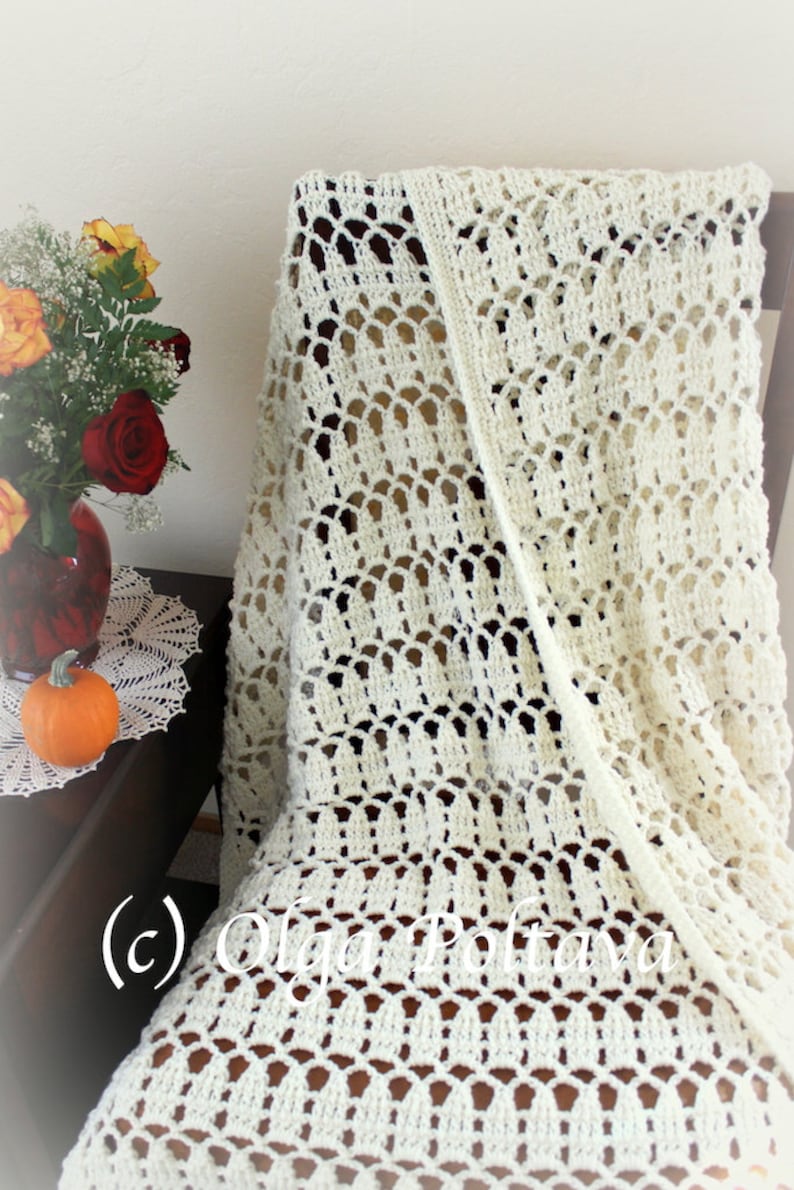 May include: A white crocheted throw blanket with a delicate, lacy pattern. The blanket is draped over a chair and has a subtle sheen.