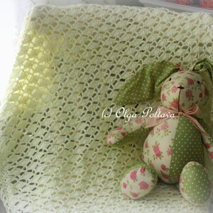 May include: A handmade, light yellow crocheted blanket with a decorative pattern. A stuffed bunny with green polka dot and floral print fabric is resting on the blanket. The bunny has long ears and a pink bow. The text "(c) Olga Poltava" is visible.