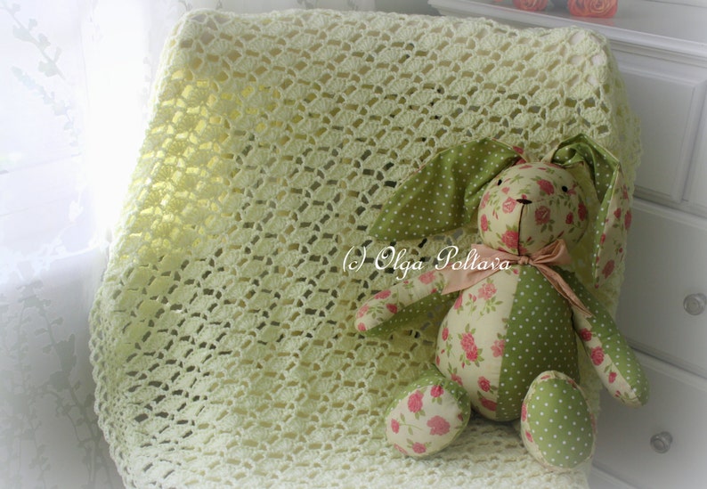 May include: A handmade, light yellow crocheted blanket with a decorative pattern. A stuffed bunny with green polka dot and floral print fabric is resting on the blanket. The bunny has long ears and a pink bow. The text "(c) Olga Poltava" is visible.