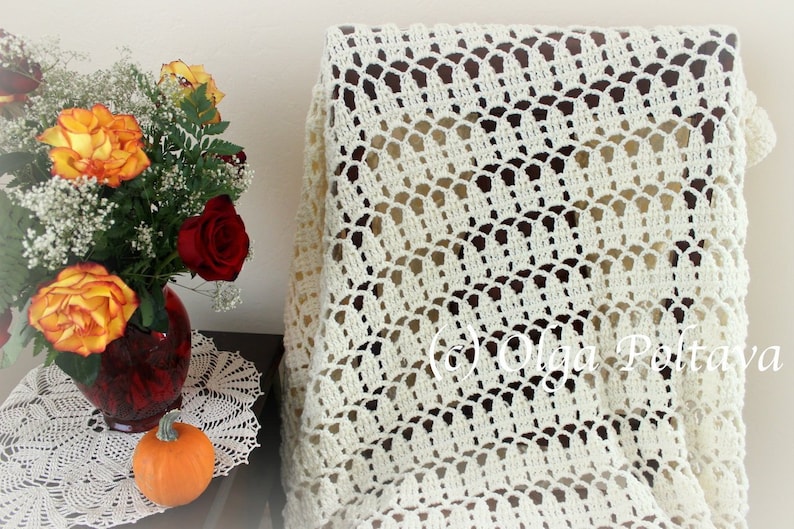 May include: A white crocheted throw blanket with a delicate, lacy pattern. The blanket is draped over a wooden chair and has a scalloped edge.