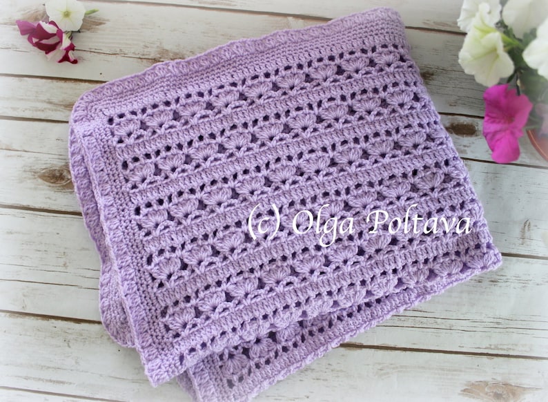 May include: A lavender crochet baby blanket with a delicate stitch pattern. The blanket is folded in half and has a scalloped edge.