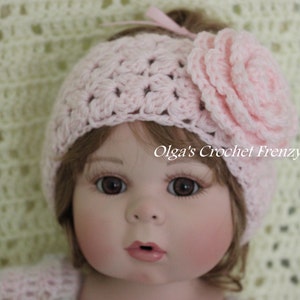 May include: A pink crocheted headband with a large pink crocheted flower on top. The headband is worn by a doll with brown hair and blue eyes.