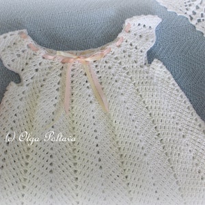 May include: White crocheted baby dress with a pink ribbon tied around the neckline. The dress has a delicate, lacy pattern and is perfect for a special occasion.