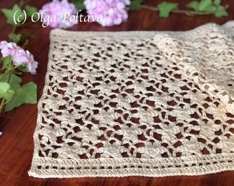 Puede incluir: Un camino de mesa de ganchillo con un delicado patrón floral en color crema. El camino de mesa está colocado sobre una mesa de madera.