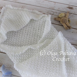 May include: White crocheted baby blanket with a scalloped edge. The blanket is folded in half and laid flat on a wooden surface. The blanket is made with a textured stitch.