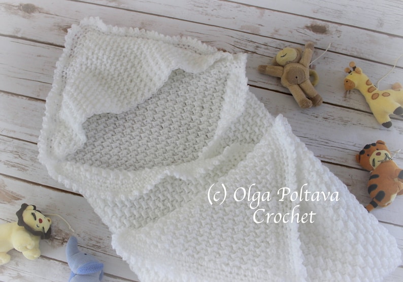 May include: White crocheted baby blanket with a scalloped edge. The blanket is folded in half and laid flat on a wooden surface. The blanket is made with a textured stitch.