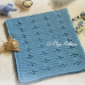 Puede incluir: Una manta de beb&eacute; de ganchillo azul claro con un patr&oacute;n de diamante. La manta est&aacute; colocada sobre una superficie blanca con algunos animales de peluche cerca.