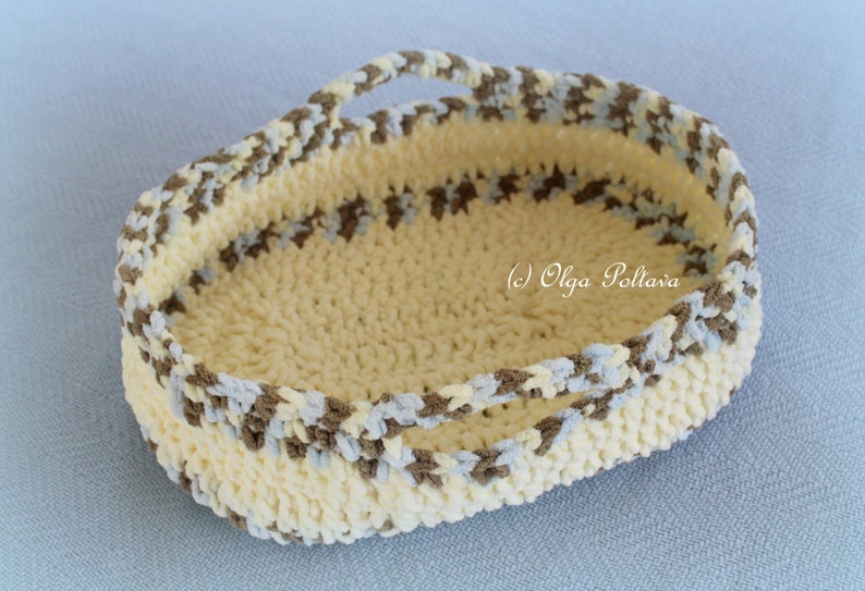 May include: A crocheted basket with a cream base and brown and blue stripes. The basket has two handles and is oval shaped.