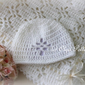 May include: White crocheted baby blanket and hat set. The blanket has a delicate lace pattern and the hat has a flower design.