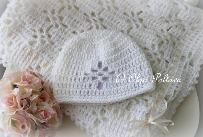 May include: White crocheted baby blanket and hat set. The blanket has a delicate lace pattern and the hat has a flower design.