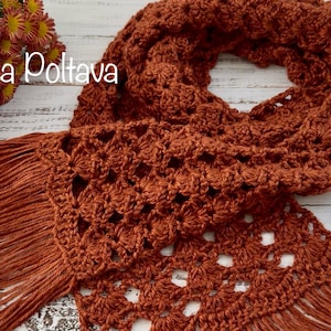 May include: A rust-colored, crocheted scarf with a fringed edge. The scarf features an openwork design and is displayed on a light-colored wooden surface. The text "(c) Olga Poltava" is visible in the image.