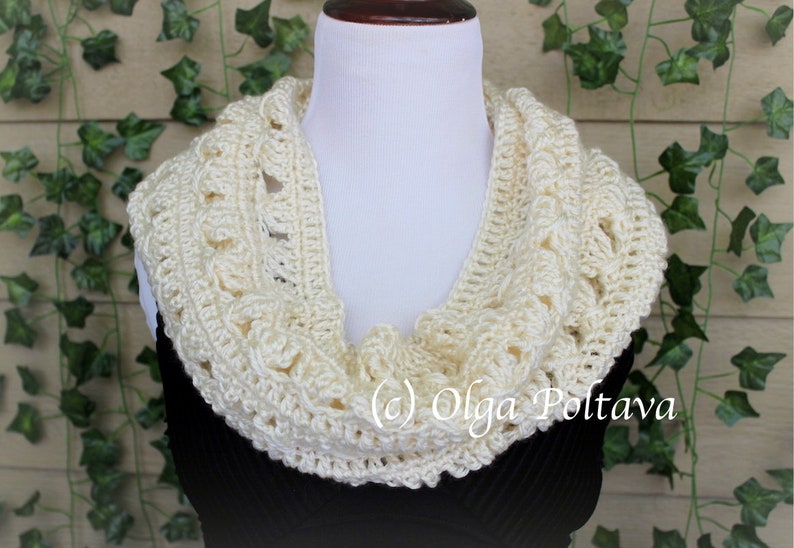 May include: A cream-colored crocheted infinity scarf featuring a textured, open-work pattern. The scarf is draped around a white mannequin neck. The text (c) Olga Poltava is visible in white lettering on the lower right side of the scarf.