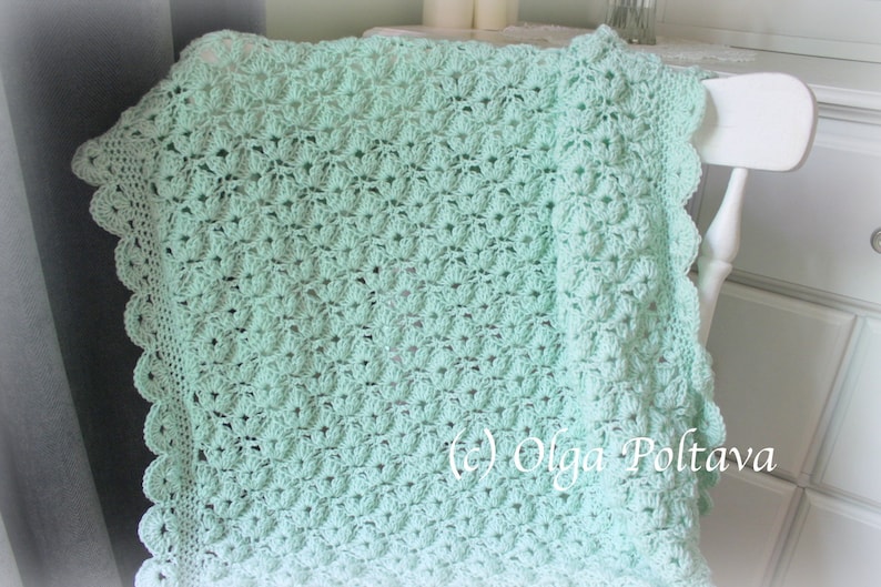 May include: A mint green crocheted blanket with a scalloped edge is draped over a white chair. The blanket features a detailed floral pattern. The image is well-lit, showcasing the texture and color of the handmade item.