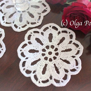 May include: Three white crocheted doilies with a floral design. The doilies are on a dark brown wooden surface. (c) Olga Poltava