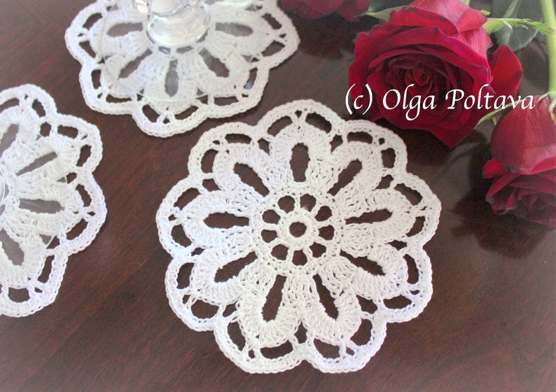 May include: Three white crocheted doilies with a floral design. The doilies are on a dark brown wooden surface. (c) Olga Poltava
