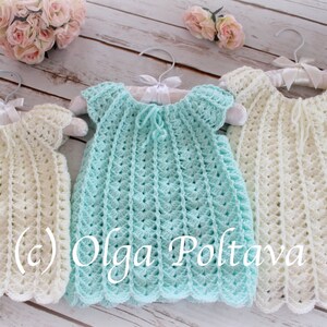 May include: Three handmade crochet dresses in cream and light blue hang on white hangers. The dresses have a scalloped hem and a textured stitch pattern. The dresses are displayed on a light wood surface with a floral arrangement in the background.