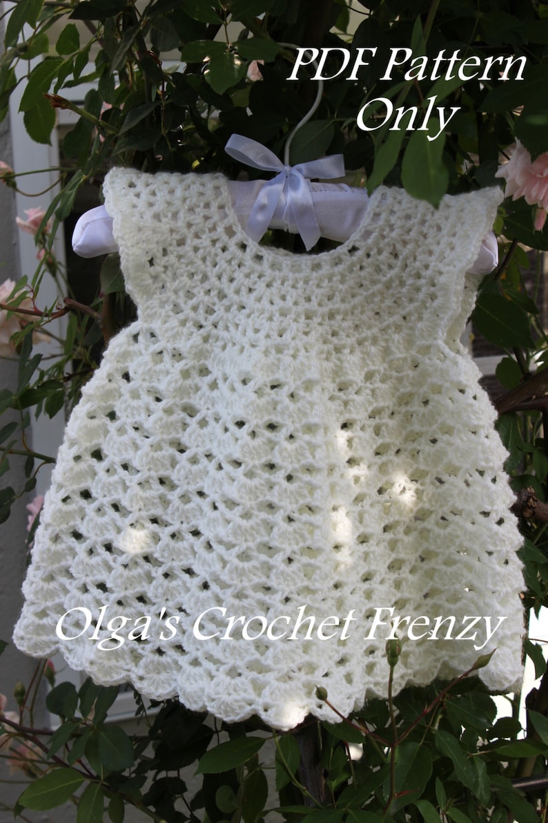 May include: White crochet baby dress with a scalloped hem. The dress is hanging on a white hanger with a white ribbon. The text "PDF Pattern Only" and "Olga's Crochet Frenzy" is visible in the image.