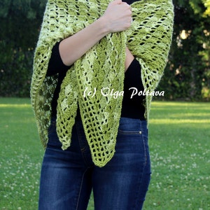 May include: A triangular crochet shawl in variegated shades of lime, olive, and forest green featuring an openwork shell stitch pattern. The shawl is draped over a black long-sleeve shirt and blue denim jeans. The text (c) Olga Poltava is visible.