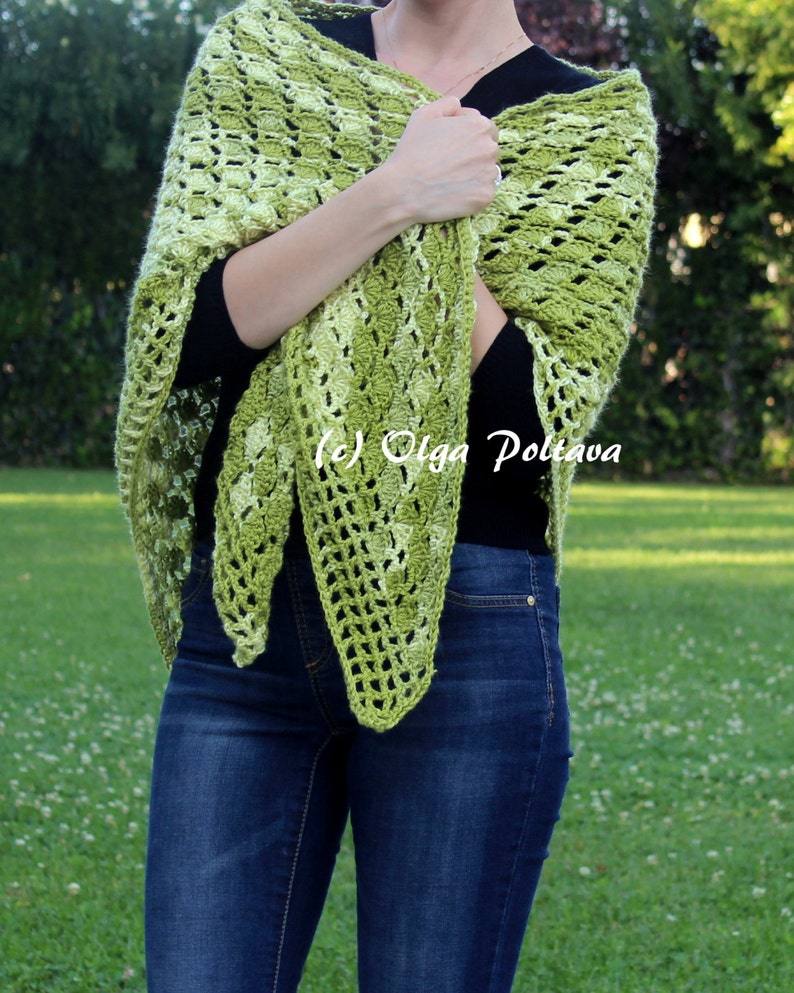 May include: A triangular crochet shawl in variegated shades of lime, olive, and forest green featuring an openwork shell stitch pattern. The shawl is draped over a black long-sleeve shirt and blue denim jeans. The text (c) Olga Poltava is visible.