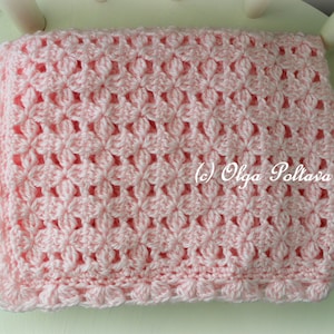 May include: A pink crocheted baby blanket with a delicate floral pattern. The blanket has a scalloped edge and is made with soft yarn.