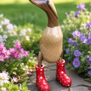 Könnte beinhalten: Eine Entenfigur aus Holz mit einem glatten, hellen Körper und einem dunkleren, polierten Kopf. Die Ente steht aufrecht und trägt leuchtend rote Gummistiefel, die mit kleinen weißen Punkten verziert sind und ein schlichtes Design aufweisen.