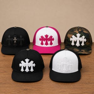 May include: Five baseball caps with mesh backs and flat brims. The caps feature a triple cross emblem on the front panels. Colors include solid black, white and pink, camouflage, black with white crosses, and white with white crosses on black.