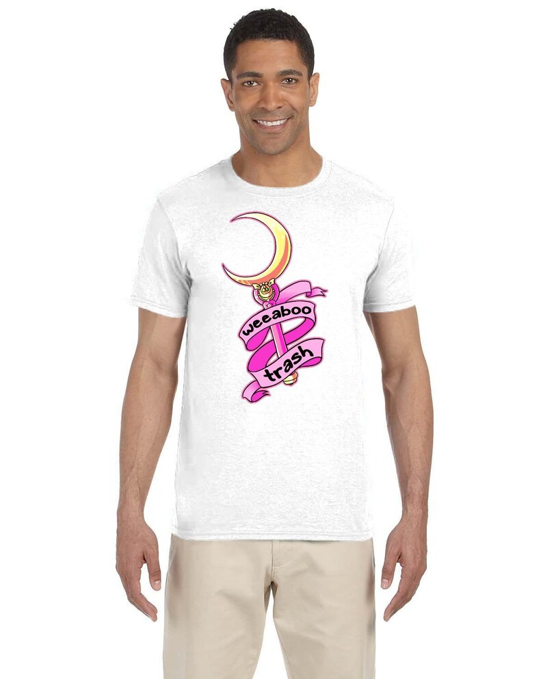 May include: White t-shirt with a pink and gold graphic of a crescent moon and a wand with the text "weeaboo trash" on a pink ribbon.