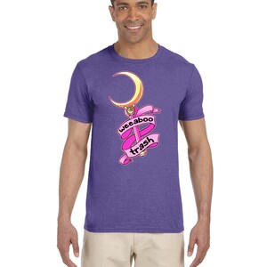 May include: A purple t-shirt with a pink and gold cartoon image of a crescent moon and wand with the text "weeboo trash" on a pink ribbon.