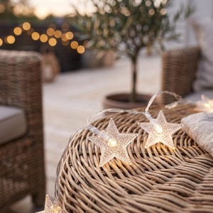 May include: A string of decorative LED lights featuring clear, textured star-shaped covers. Each star contains a small, warm-toned light bulb. The lights are connected by a thin, flexible transparent wire, creating a soft glow across the surface.