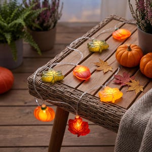 May include: A string of decorative LED lights featuring translucent, glowing shapes of autumn leaves, pumpkins, and acorns. The lights are connected by a thin, clear wire and emit a warm, soft glow, showcasing various fall-themed designs.