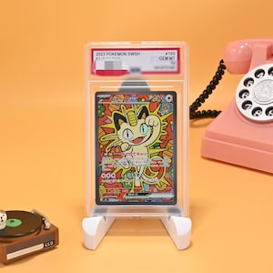 May include: A graded 2023 Pokemon SWSH #160 Meowth ex trading card in a clear plastic slab. The card features a colorful, stylized illustration of the character Meowth against a vibrant orange and yellow background with Japanese text throughout.