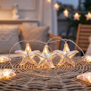 May include: A string of decorative LED lights featuring translucent, iridescent starfish-shaped covers. Each starfish has a textured, dotted surface and emits a warm, glowing light from within. The lights are connected by a thin, flexible wire.