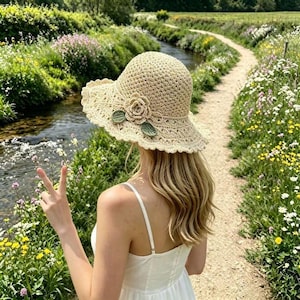 May include: A beige crochet sun hat featuring a wide, scalloped brim and a decorative three-dimensional crocheted flower accent with two green leaves attached to the side of the crown, crafted from a textured, woven yarn material.