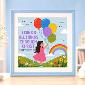 May include: A framed cross-stitch artwork featuring a child in a pink dress holding a bunch of red, blue, yellow, purple, and green balloons. The text reads I CAN DO ALL THINGS THROUGH CHRIST PHILIPPIANS 4:13 above a rainbow and green hills.