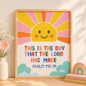 Pode incluir: Uma peça de arte em ponto cruz emoldurada com um sol amarelo sorridente com raios cor-de-rosa e laranja. Abaixo do sol, o texto diz: THIS IS THE DAY THAT THE LORD HAS MADE PSALM 118:24 em letras multicoloridas sobre nuvens azul-claras.