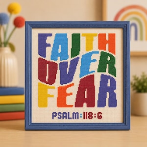 Pode incluir: Um bordado em ponto cruz quadrado numa moldura azul com o texto FAITH OVER FEAR em letras de bloco arrojadas e multicoloridas sobre um fundo de tecido creme. Abaixo do texto principal, as palavras PSALM 118:6 estão bordadas em azul e vermelho.
