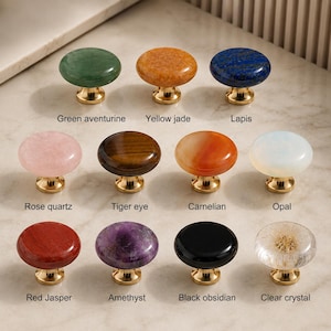May include: A collection of eleven round cabinet knobs with gold-toned metal bases, each featuring a different gemstone or material top: green aventurine, yellow jade, lapis, rose quartz, tiger eye, carnelian, opal, red jasper, amethyst, black obsidian, and clear crystal.