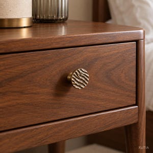 May include: A dark brown wooden nightstand featuring a single drawer with a round, textured brass knob. The knob has a wavy, rippled surface pattern. The wood grain is visible across the drawer front and the top surface of the furniture piece.