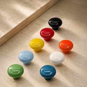 Puede incluir: Una colección de ocho pomos redondos para armarios con un acabado liso y brillante. Los pomos están disponibles en una variedad de colores sólidos, incluyendo negro, rojo, amarillo, naranja, azul claro, blanco, verde y azul oscuro.