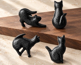 Op de afbeelding: Vier zwarte katvormige kastknoppen met een textuurafwerking. Twee katten zijn van achteren zittend afgebeeld, één rekt zich uit en één staat in profiel. Het woord XUTIA staat in de rechterbenedenhoek gedrukt.