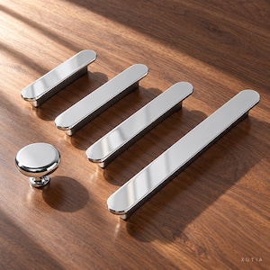 May include: A collection of polished chrome cabinet hardware including one round knob and three elongated rectangular pulls of varying lengths, all featuring a smooth, reflective metallic finish and rounded edges.